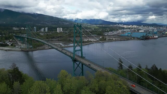 Aerial shot over Lions Gate Bridge in Vancouver city with north vancouver mountains in the background and stanley park in the foreground on a cloudy day in British Columbia, Canada