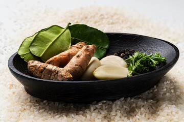 A variety of spices in a wooden bowl placed over a bed of raw white rice, Asian culinary ingredients