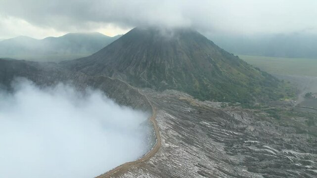 Aerial view of volcano crater emitting thick white smoke and mountain surrounded by mist on background. Concept of epic, dramatic wild nature landscapes. East Java, Bromo