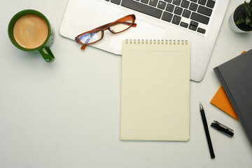 Flat lay of workspace with laptop, notebook, glasses and a coffee cup on white background