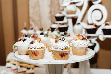 cupcakes placed on a white stand. The cupcakes are decorated with white frosting and a variety of berries such as blackberries and raspberries, as well as fruit pieces and green leaves.