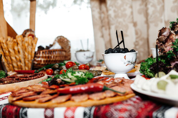 dish with cold cuts. Various types of sausages and meats are laid out on a round wooden plate, garnished with herbs and small cherry tomatoes. In the center of the dish are pieces of sausage surrounde