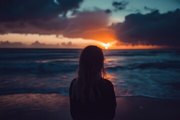 Fototapeta premium A person standing alone on a beach during sunset