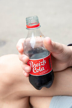 Petite bouteille en plastique de boisson gazeuse Breizh Cola Bretagne avec logo. La bouteille est tenue dans une main, gros plan, France.