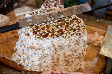 Grosse portion de nougat traditionnel (miel, amande, pistache, noisette, blanc oeuf, sucre) à découper dans un magasin en France.