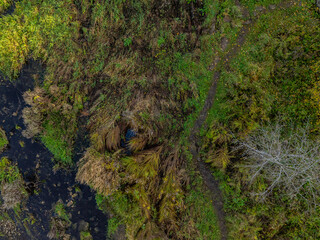 Top-down aerial photo of the Jagala River near Jägala Waterfall in Estonia. On the left the river flows with dark, almost black water speckled with white foam. On the right rugged green landscape.