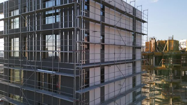 Construction of a modern multi-story building with scaffolding in a busy urban area at sunset