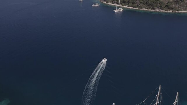 A drone follows a small white boat on a crystal clear sea.