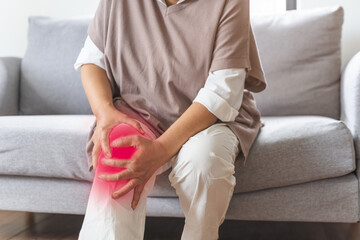 Body arthritis muscles stiff problem, aged woman suffering on leg, pain knee from disease chronic, hand massage rubbing joint injury, mature hurt or sore sitting on sofa at home. Health care people.