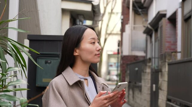 路地で待ち合わせをしながらスマホを操作する女性（A woman operating her smartphone while waiting for someone in an alley）