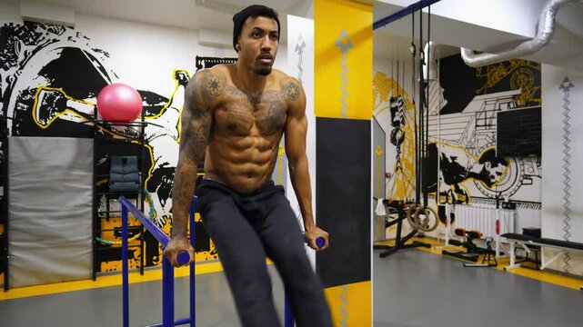 Strong black guy training abdominal muscles on parallel bars at gym. Afro american sportsman exercising at sport club. Muscular african athlete working out at fitness centre. Healthy lifestyle concept