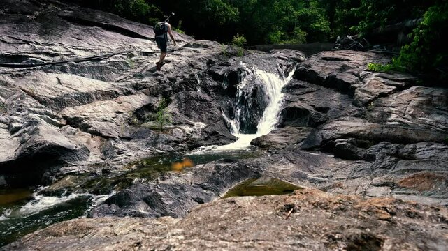 A tourist along a mountain stream climbs along the riverbed in the jungle