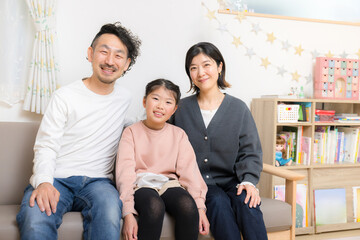 自宅で過ごす小学生の子供と夫婦の3人家族のイメージ　カメラ目線の笑顔