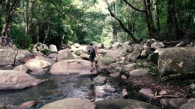 A tourist moves from stone to stone in the bed of a mountain river in the jungle