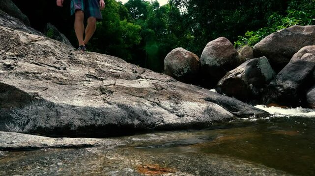 A tourist walks down the rocks in the jungle past a stream