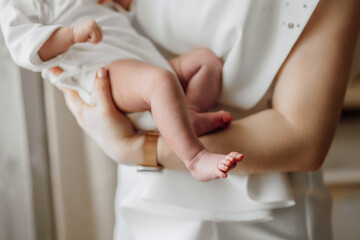 A woman is holding a baby in her arms. The baby is wearing a white outfit. The woman is holding the baby's foot