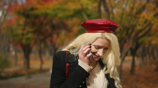Blonde woman smiling while speaking on phone walking in Forest Park, colorful autumn backdrop, medium closeup frontal tracking