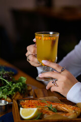 the girl holds a glass of sea buckthorn and rosehip tea in her hands