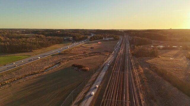 Rail tracks and a motorway at sunset, high speed train passing by, cars on the motorway. E4 between Stockholm and Arlanda airport.