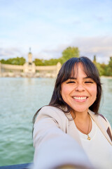 Smiling Latina woman taking a selfie by a lake with a historic monument in the background