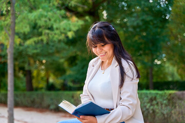 Obraz premium Latina woman reading a book while sitting on a bench in a peaceful park