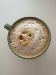 a green coffee mug with thick milk foam on a white table. View from above. Vertical photo