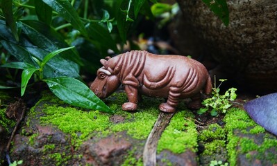 hippo toy, children's toy, brown hippo animal in mossy rock photo, looks real and unique