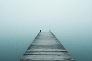 Obraz premium A lone pier stretches out over still, fog-covered water, creating a serene and mysterious atmosphere as if disappearing into infinity on a foggy day.