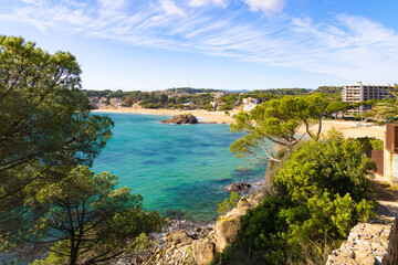 Obraz premium Bahía con agua turquesa, playa dorada, rocas y vegetación mediterránea en La Fosca.