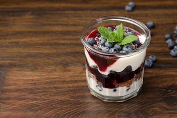 Tasty trifle dessert. Blueberries, sponge cake and whipped cream in glass on wooden table, space for text