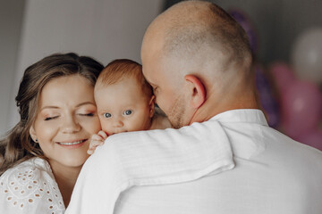 A man and a woman are holding a baby. The baby is smiling and the man is kissing the baby's head....