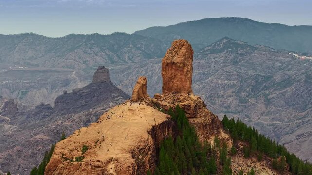 Stunning view of Roque Nublo at sunset with dramatic rock formations and mountainous landscape in Gran Canaria. Aerial shot of tourists walk on the cliff of Roque Nublo. 4K telephoto