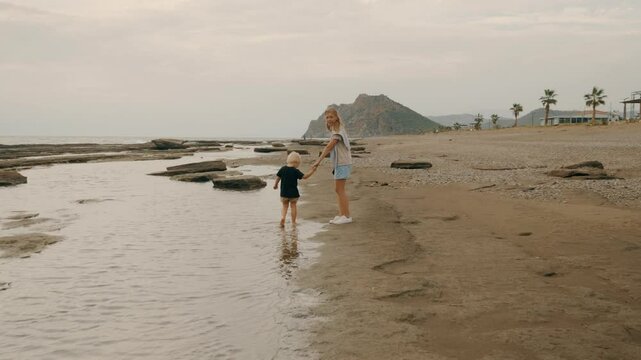Young mother and son kid walking at sand beach seaside relaxing outdoor spending time together