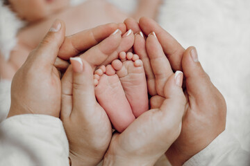 A baby is being held by a couple, with their hands around the baby's feet. Concept of warmth, love, and protection, as the couple embraces the baby