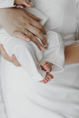 A woman is holding a baby in her arms. The baby is wearing a white outfit and has a ring on its finger. Concept of warmth and love between the mother and her child