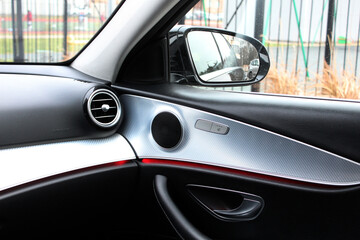 Car interior with view of air conditioner vent and side view mirror. Front Airbag. Vent for air flow in passenger side. Sound speaker in a modern car door panel. Close up car speaker on car door panel