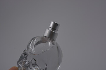 Objects, things, cosmetics and perfumes. A beautiful transparent glass bottle of women's perfume in the shape of a skull with silver spray is located on a white plastic background.