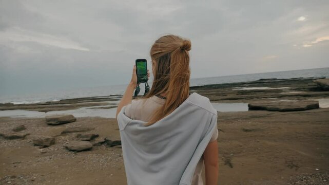 Redhead touristic woman shooting sea wave video camera use smartphone display back view slow motion