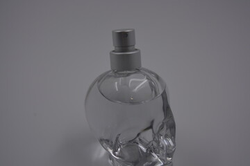 Objects, things, cosmetics and perfumes. A beautiful transparent glass bottle of women's perfume in the shape of a skull with silver spray is located on a white plastic background.