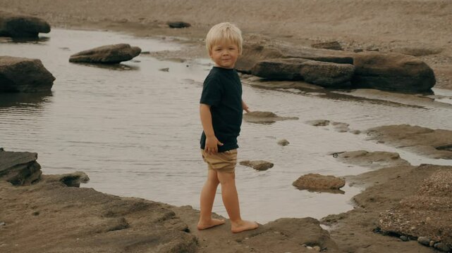 Male blonde kid walking sea stone sand beach relaxing outdoor enjoy summer travel vacation
