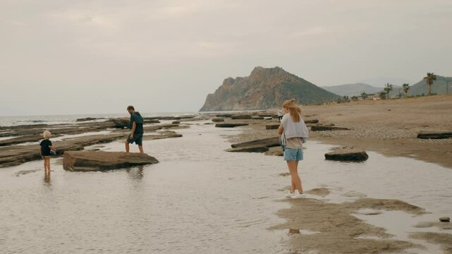 Man woman and kid son walking sea beach stones seaside resort landscape with palm trees slow motion