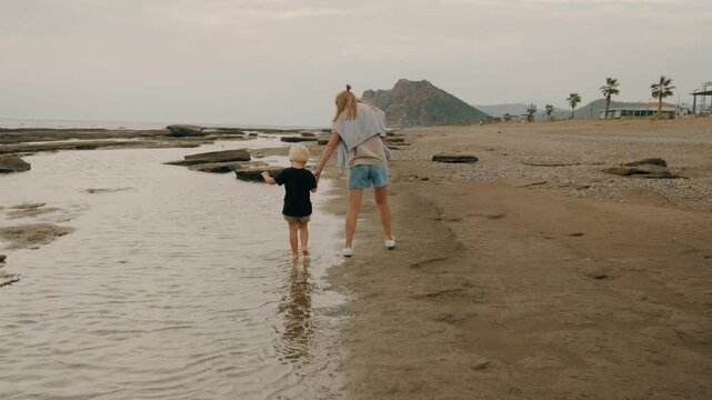 Travel mother and son walking at sand sea beach together holding hands enjoy summer vacation slowmo