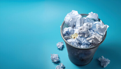 Metal trash bin full of crumpled paper on blue background. Overflowing waste paper basket.