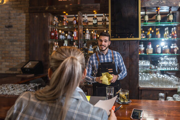 Satisfied restaurant owner checking monthly reports on laptop, bills and expenses of her small business. Start-up entrepreneur happy about financial reports while talking to the waiter or barman.
