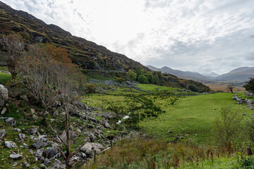 Elevated view of a valley, with rolling hills, grassy fields, and rocky outcrops.  A stream meanders through the landscape.