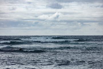 Ocean waves under a cloudy sky.  Rough water, light gray clouds.  Calm, overcast day.