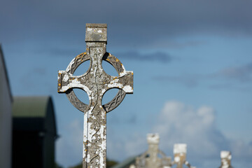 Weathered Celtic cross, likely a gravestone,  against a partly cloudy sky.  Details carved into the...