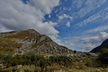 Rocky mountainside with varied vegetation.  Cloudy sky above.  A small body of water is visible in the foreground.