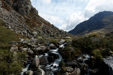 Mountainous landscape with a cascading waterfall.  Rocks, vegetation, and a rushing stream fill the valley.