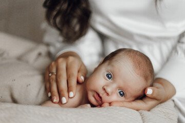 A woman is holding a baby in her arms. The baby has blue eyes and is laying on a bed. The woman is looking at the baby with a smile on her face